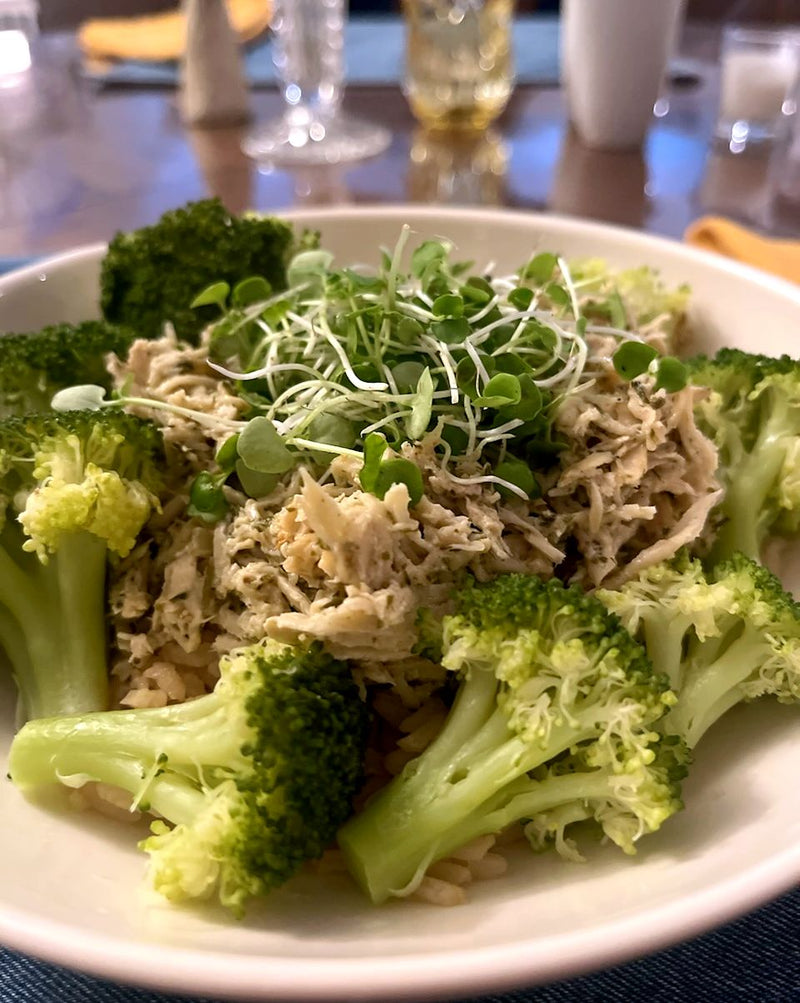 Shredded chicken and rice bowl with broccoli, topped with a handful of fresh microgreens